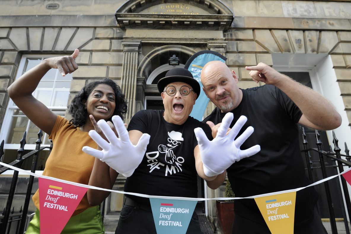 Three people standing in front of Edinburgh Deaf Festival bunting