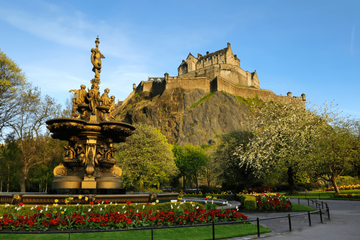 edinburgh castle on top of hill with fountain surrounded by red flowers in foreground